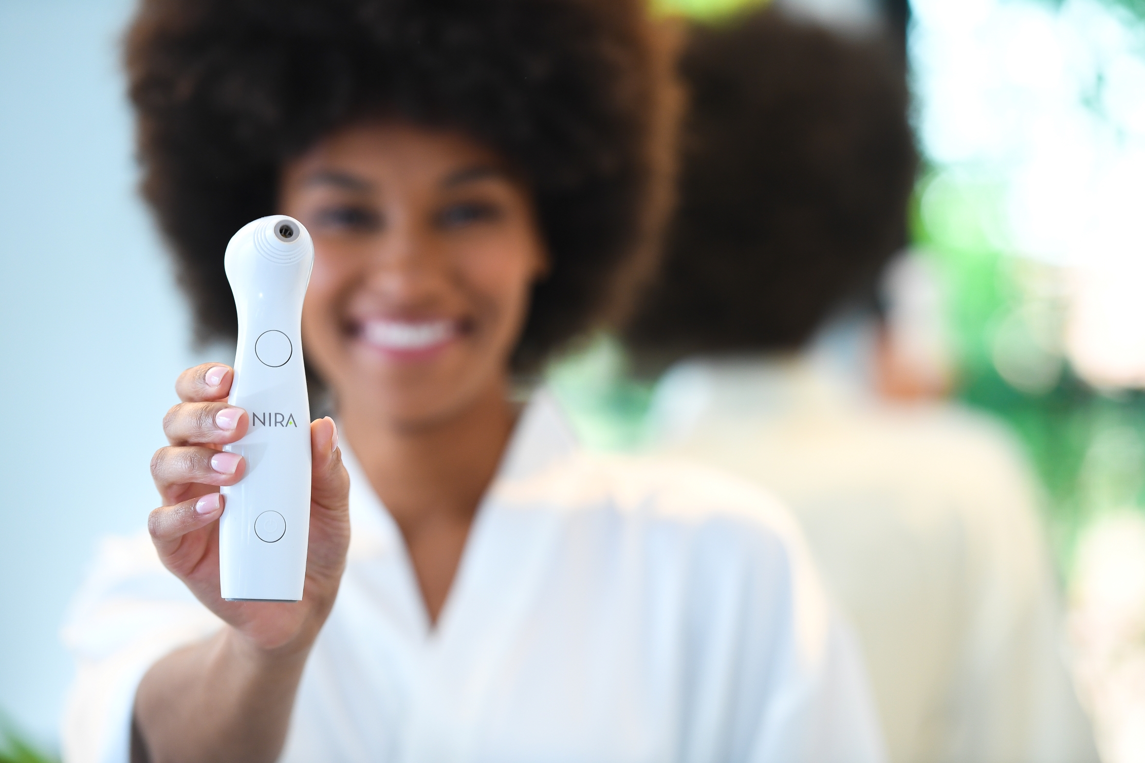Smiling woman holds a NIRA laser skincare device toward the camera, highlighting an easy, noninvasive solution for smoother skin