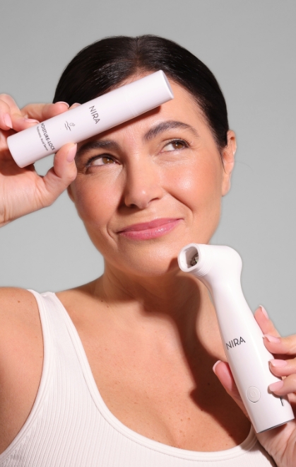 Woman holding NIRA laser device and skincare serum against gray background, showcasing anti-aging beauty tools.