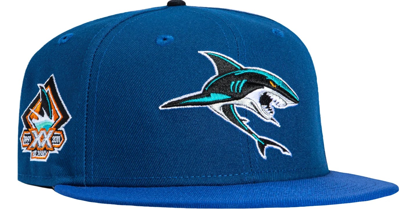 Blue fitted baseball cap with embroidered shark logo and side patch displayed on white background, featuring Hat Club detailing