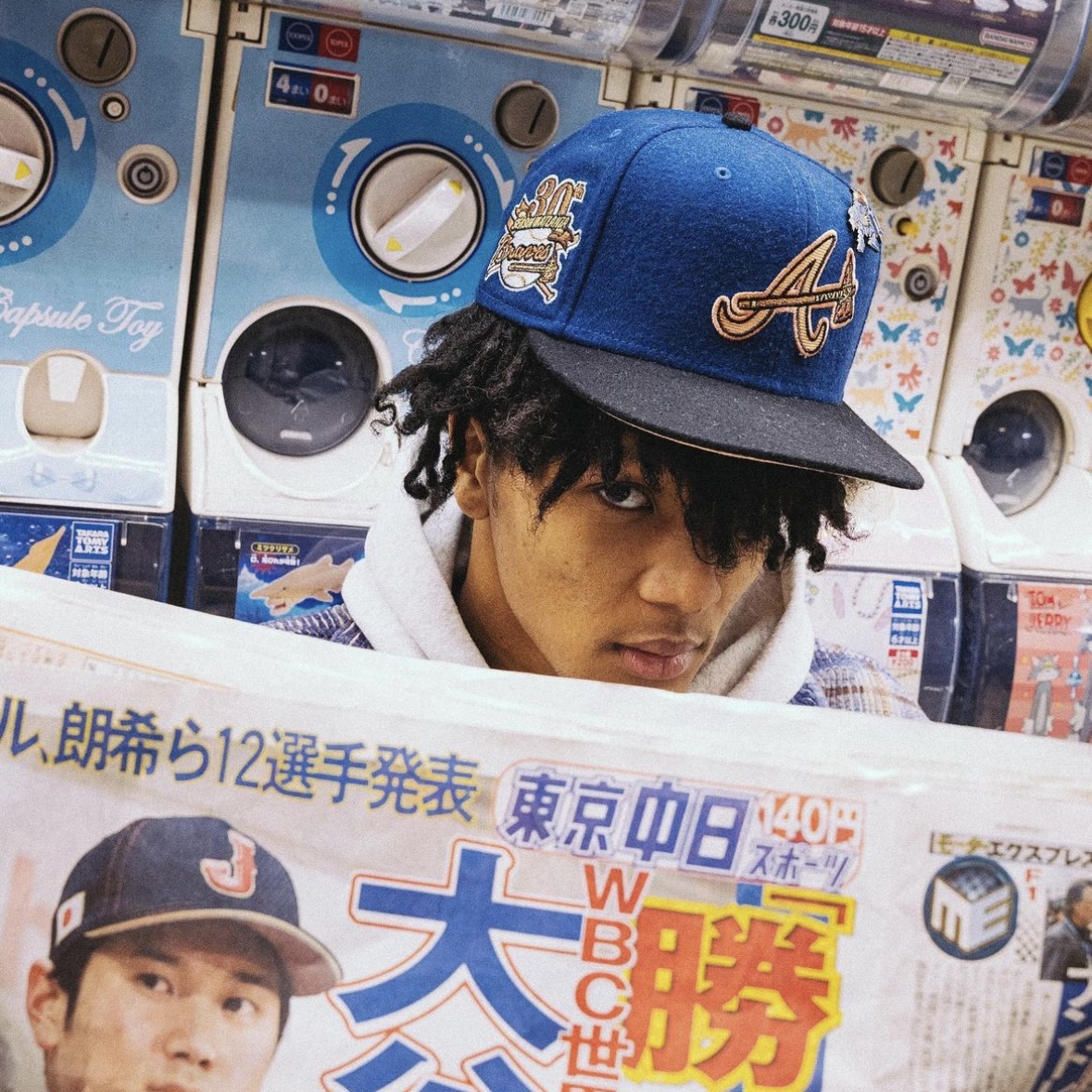 Person wearing a blue Atlanta Braves fitted cap poses in front of capsule machines, blending streetwear style with Hat Club gear